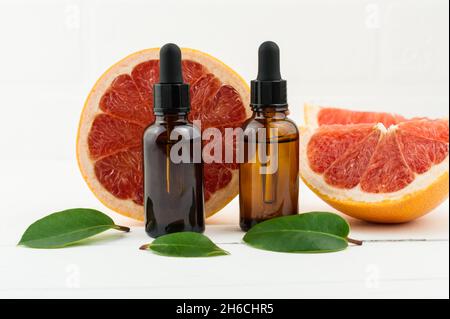 Zwei Flaschen Tropferflaschen mit kosmetischem Grapefruitöl oder Gesichtsserum vor dem Hintergrund frischer Grapefruitfrüchte. Ein natürliches Konzept der Selbstpflege Stockfoto