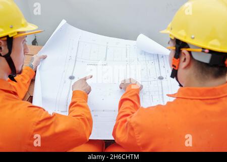 Bauherren in Hardhats, die auf den Bauplan zeigen, Blick von hinten Stockfoto