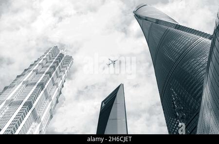 Dramatisches Schwarz-Weiß-Bild eines Flugzeugs, das über moderne Gebäude und Wolkenkratzer in Shanghai, China, fliegt Stockfoto