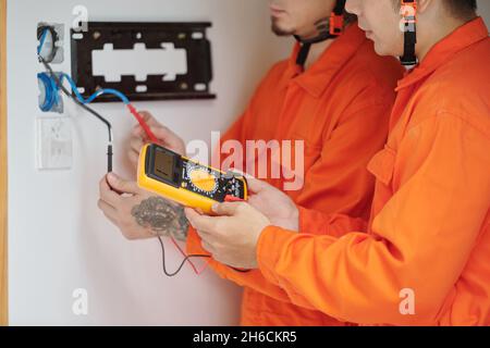 Hände von Elektrikern, die Multimeter verwenden, wenn sie die Verkabelung im Haus reparieren und ein neues Multimeter installieren Stockfoto