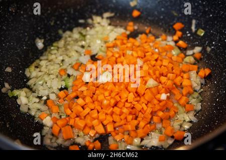 Nahaufnahme von Zwiebel und Karotte zum Kochen von Bolognese-Sauce in der Pfanne auf Induktionsherd in der Küche Stockfoto