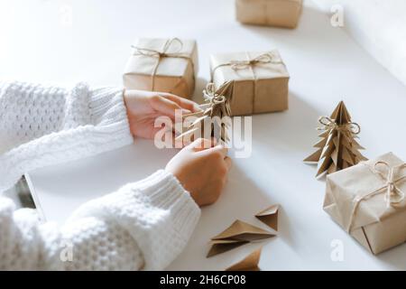 Das Kind bereitet sich auf Weihnachten vor, verpackt Geschenke und macht aus Papier ein Origami-Handwerk. DIY-Konzept Stockfoto