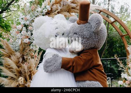 Ein paar Teddybär-Animateure umarmen sich auf dem Hintergrund des Hochzeitsbogens Stockfoto