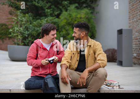 Glücklicher junger Mann mit Down-Syndrom und Mentoring-Freund im Freien sitzen Stockfoto