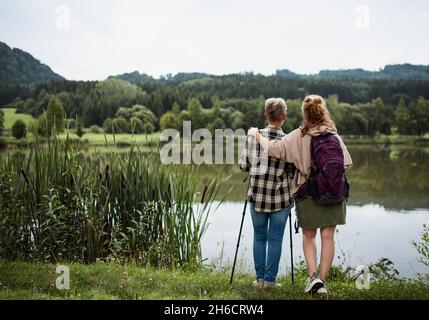 Rückansicht der älteren Mutter, die sich mit der erwachsenen Tochter umarmt, wenn sie im Freien am See in der Natur steht Stockfoto