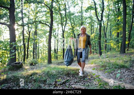 Ältere Ökologin mit Müllbeutel, die im Wald Abfälle aufsammeln. Stockfoto
