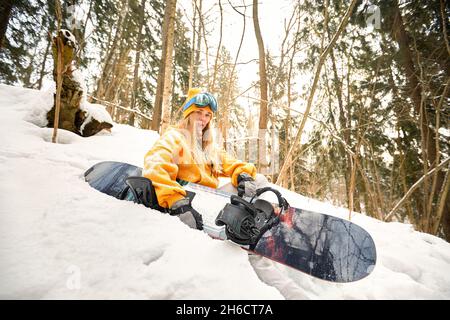 Kaukasische Frau Snowboarderin hält Snowboard auf schönen verschneiten Wald Hintergrund an sonnigen Tagen Stockfoto