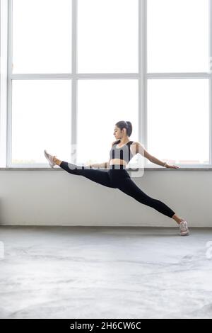 Junge attraktive Frau, die Yoga-Konzept praktiziert, in Variation der Pincha Mayurasana-Übung steht, Handstandhaltung, trainiert, Sportkleidung trägt, Stockfoto