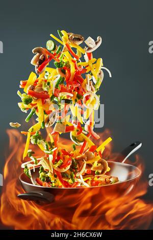 Bratpfanne Wok mit Gemüse in der Luft auf Feuer. Gemüsewok - Paprika, Zwiebeln, Erbsen, Pilze, Bohnen, Brokkoli, Zucchini. Asiatische Küche. Chinesisches f Stockfoto