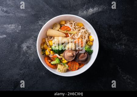 Draufsicht auf Teller mit asiatischen Nudeln, Mais, Brokkoli, Karotten und Shiitake-Pilzen auf schwarzem Marmorhintergrund Stockfoto