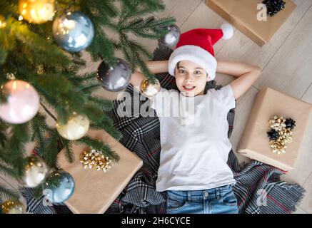 Der Junge liegt unter dem Baum und träumt. Weihnachtsbaum im großen Wohnzimmer. Stockfoto