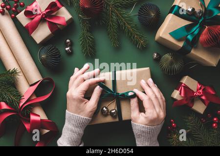 Overhead-Ansicht auf weiblichen Händen binden Samtband auf Weihnachten Geschenkbox auf grünem Hintergrund. Stockfoto