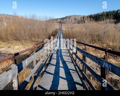 Hängebrücke auf Eisenseilen über das Herbsttal mit einem kleinen Fluss Stockfoto