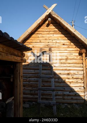 Die Wand eines Holzhauses im Dorf mit einer Leiter, die sich daran lehnt Stockfoto