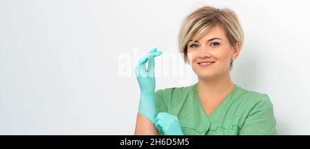 Arzt Kosmetikerin setzt auf sterile blaue Handschuhe lächelnd bereitet sich auf Kunden auf weiß zu empfangen Stockfoto