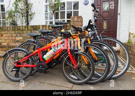 Vier Fahrräder / Fahrräder / 4 Fahrräder gesperrt Verkauf vor dem Haus einer Fahrrad-Reiten-Familie. Das Fahrradschloss ist an der Gartenwand befestigt. VEREINIGTES KÖNIGREICH (127) Stockfoto