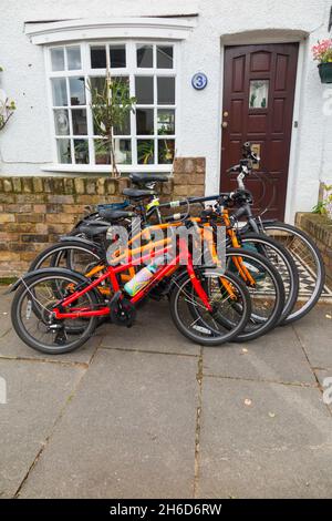 Vier Fahrräder / Fahrräder / 4 Fahrräder gesperrt Verkauf vor dem Haus einer Fahrrad-Reiten-Familie. Das Fahrradschloss ist an der Gartenwand befestigt. VEREINIGTES KÖNIGREICH (127) Stockfoto