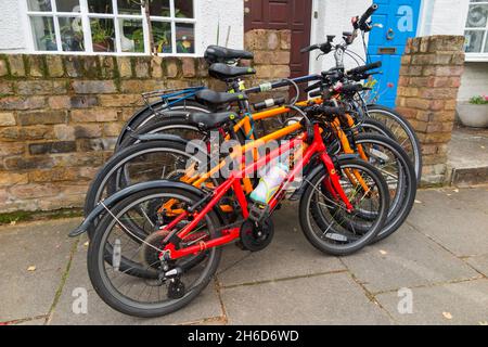 Vier Fahrräder / Fahrräder / 4 Fahrräder gesperrt Verkauf vor dem Haus einer Fahrrad-Reiten-Familie. Das Fahrradschloss ist an der Gartenwand befestigt. VEREINIGTES KÖNIGREICH (127) Stockfoto