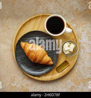 Frühstück Croissant, schwarzer Kaffee und Butter auf Holzplatte auf Marmortisch Stockfoto