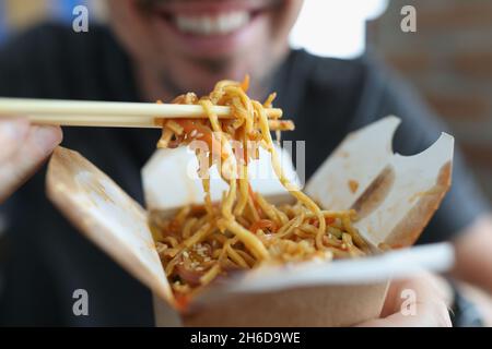 Lächelnder Mann, der würzige Nudel isst chinesisches Essen mit Gemüse mit Essstäbchen Stockfoto