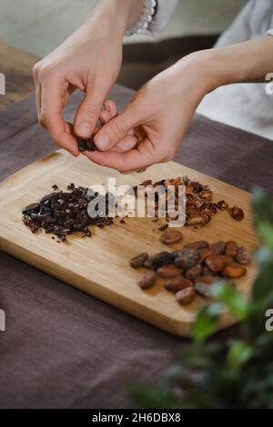 Hände schälen Bio-Kakaobohnen auf Holztisch, Kakaobohnen, handwerkliche Schokolade in rustikalem Stil für die Zeremonie auf dem Tisch. Degustation Stockfoto