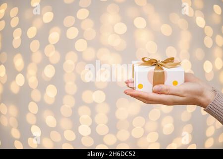 Frau mit einem weißen Geschenkkarton mit einer goldenen Schleife Auf einem hellen Feiertagslicht Hintergrund Stockfoto