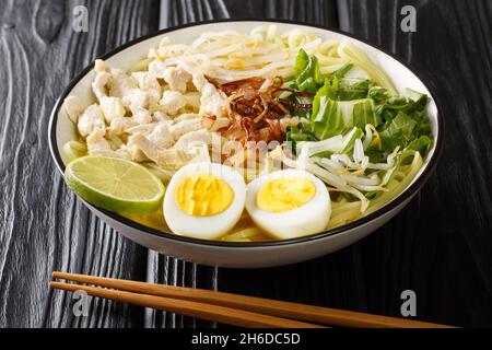 Indonesische Hühnernudelsuppe „Soto Ayam“ in einer würzigen Brühe in Nahaufnahme auf dem Teller auf dem Tisch. Horizontal Stockfoto