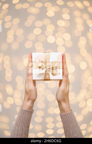 Frau mit einem weißen Geschenkkarton mit einer goldenen Schleife Auf einem hellen Feiertagslicht Hintergrund Stockfoto