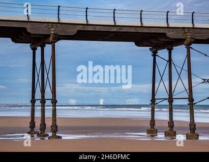 Die Windturbinen von Redcar durch die Eisenstützen des Saltburn Pier, North Yorkshire, England Stockfoto