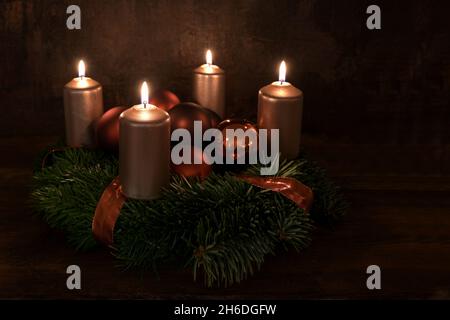 Kleiner Adventskranz mit vier beleuchteten kupferfarbenen Kerzen und Weihnachtsdekorkugeln vor dunkelbraunem rustikalem Hintergrund, Kopierraum, ausgewählt Stockfoto