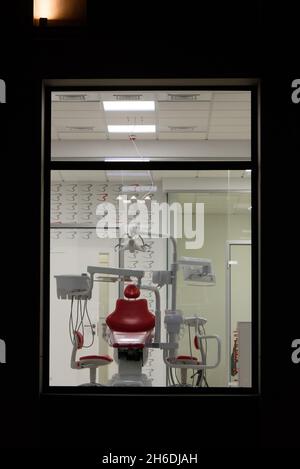 Neue Zahnarztpraxis. Nachtzahnmedizin. Roter Zahnstuhl, Blick durch das Fenster Stockfoto