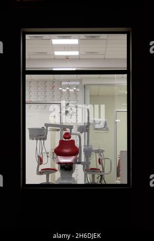 Neue Zahnarztpraxis. Nachtzahnmedizin. Roter Zahnstuhl, Blick durch das Fenster Stockfoto