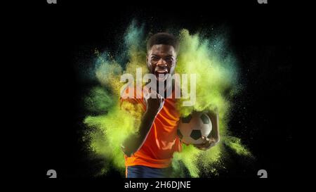 Collage mit jungen Sportlern, Fußballspieler in Explosion von farbigem Neonpulver isoliert auf dunklem Hintergrund Stockfoto