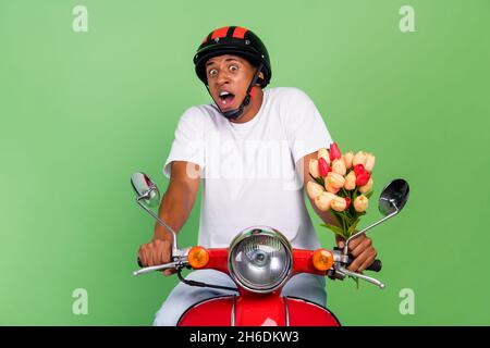 Foto von jungen Afro-Mann Angst besorgt halten Haufen von Tulpen fahren Motorrad isoliert über grünen Hintergrund Stockfoto