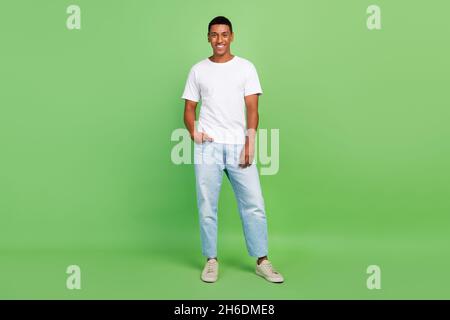 In voller Länge Foto von jungen afro Mann gute Laune Arm in der Tasche tragen Freizeitkleidung isoliert über grünen Hintergrund Stockfoto