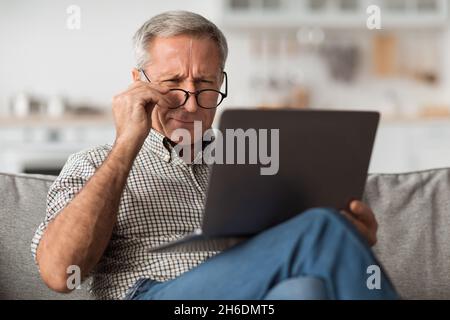 Ältere Männliche Augenblinzeln Mit Laptop Tragen Brillen Zu Hause Stockfoto