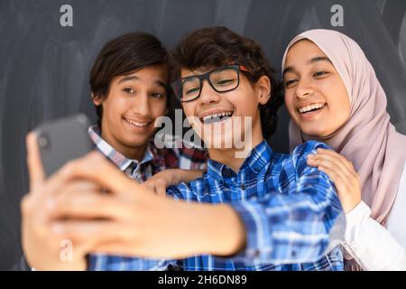Gruppe von arabischen Teenagern, die Selfie-Fotos auf dem Smartphone mit schwarzer Tafel im Hintergrund machen. Selektiver Fokus Stockfoto