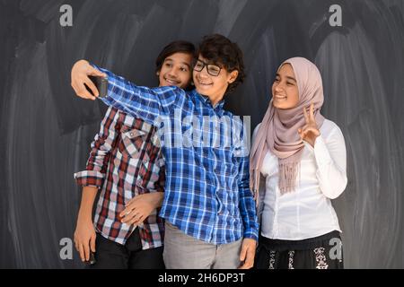 Gruppe von arabischen Teenagern, die Selfie-Fotos auf dem Smartphone mit schwarzer Tafel im Hintergrund machen. Selektiver Fokus Stockfoto