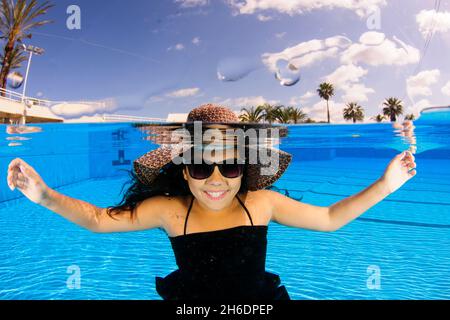 Eine 12-jährige weibliche Teenager, die unter Wasser in einem Swimmingpool mit Sommerhut frei tauchen kann Stockfoto