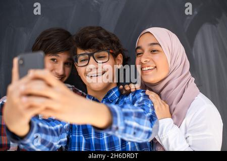 Gruppe von arabischen Teenagern, die Selfie-Fotos auf dem Smartphone mit schwarzer Tafel im Hintergrund machen. Selektiver Fokus Stockfoto