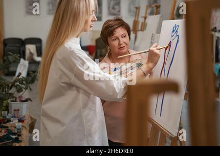 Niedlicher langhaariger Maler, der Farben auf der Palette mischt Stockfoto