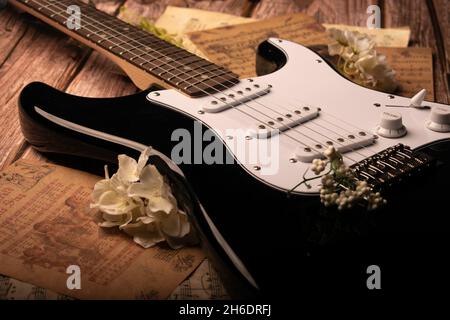 Stillleben Foto eines Fender Squier Stratocaster legte auf Noten umgeben von Blumen. Aufgenommen mit geringer Schärfentiefe. Stockfoto