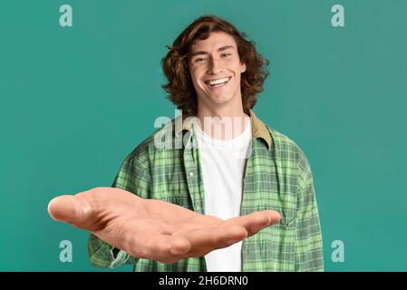Fröhlicher Kerl im lässigen Outfit, der die Hand auf Türkis ausstreckt Stockfoto