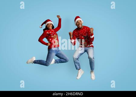 Fröhliches schwarzes Paar in Weihnachtsmützen, das Erfolg feiert Stockfoto
