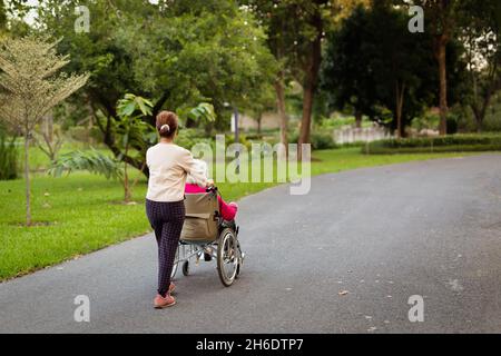 Hausmeister schiebt ältere Frau im Park in einen Rollstuhl. Stockfoto