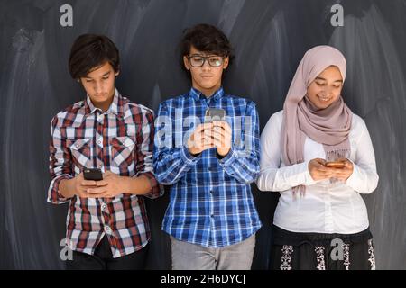 Gruppe von arabischen Teenagern, die Selfie-Fotos auf dem Smartphone mit schwarzer Tafel im Hintergrund machen. Selektiver Fokus Stockfoto