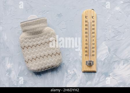 Thermometer zeigt niedrige Temperatur und Mini-Silikon-Heißwasserflasche mit gestricktem Deckel für die Hand- oder Körpererwärmung auf weißem und blauem Hintergrund. Warm halten im Winter Outdoor-Konzept, kopieren Platz