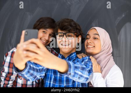 Gruppe von arabischen Teenagern, die Selfie-Fotos auf dem Smartphone mit schwarzer Tafel im Hintergrund machen. Selektiver Fokus Stockfoto