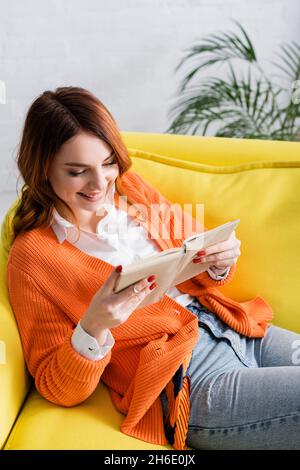 High-Angle-Ansicht der fröhlichen Frau Buch auf der gelben Couch lesen Stockfoto