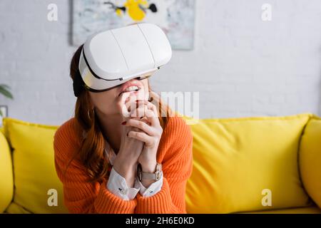 Besorgte Frau mit geballten Händen, die zu Hause im VR-Headset spielen Stockfoto